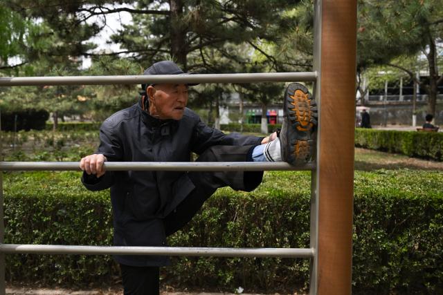 An elderly man stretches in a public park in Beijing on April 12, 2026. (Photo by Pedro PARDO / AFP)