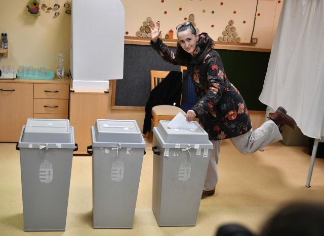 A woman waves to photographers as she casts her ballot at a polling station in Budapest at the start of a general election in Hungary, on April 12, 2026. The vote could end Hungarian Prime Minister Viktor Orban's 16-year stint in power as the EU's longest serving current leader and a self-decribed "thorn" in the bloc's side. (Photo by Ferenc ISZA / AFP)