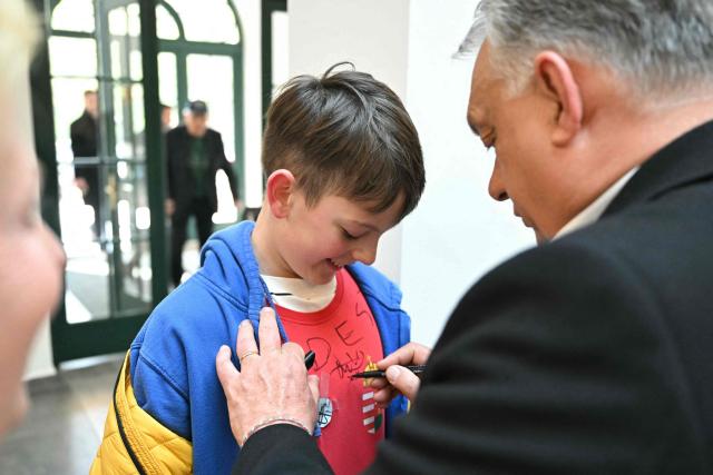 Hungary's nationalist Prime Minister Viktor Orban (R) of the Fidesz party signs a young boy's t-shirt after voting at a polling station set up in a school in Budapest during a general election in Hungary, on April 12, 2026. The vote could end Hungarian Prime Minister Viktor Orban's 16-year stint in power as the EU's longest serving current leader and a self-decribed "thorn" in the bloc's side. (Photo by Attila KISBENEDEK / AFP)
