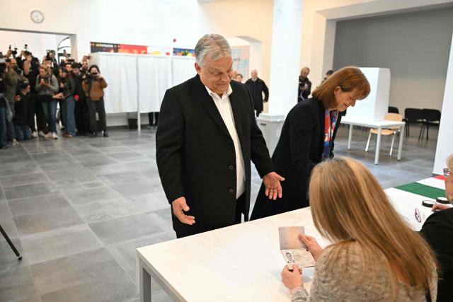 Hungarian Prime Minister Viktor Orban (L) presents his passport beside his wife Aniko Levai (R) at a polling station set up in a school of the 12th district in Budapest during a general election in Hungary, on April 12, 2026. The vote could end Hungarian Prime Minister Viktor Orban's 16-year stint in power as the EU's longest serving current leader and a self-decribed "thorn" in the bloc's side. (Photo by Attila KISBENEDEK / AFP)
