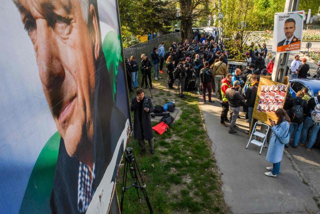Peter Magyar (background, C), leader of the pro-European conservative TISZA party, talks with journalists after casting his ballot at a polling station in Budapest, as in foreground (L) can be seen an election poster of Hungary's nationalist Prime Minister Viktor Orban of the Fidesz party during a general election in Hungary, on April 12, 2026. The vote could end Hungarian Prime Minister Viktor Orban's 16-year stint in power as the EU's longest serving current leader and a self-decribed "thorn" in the bloc's side. (Photo by Ferenc ISZA / AFP)