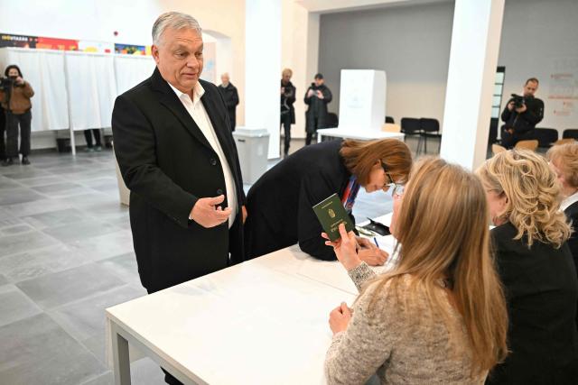 Hungarian Prime Minister Viktor Orban (L) presents his passport beside his wife Aniko Levai (standing next to him) at a polling station set up in a school of the 12th district in Budapest during a general election in Hungary, on April 12, 2026. The vote could end Hungarian Prime Minister Viktor Orban's 16-year stint in power as the EU's longest serving current leader and a self-decribed "thorn" in the bloc's side. (Photo by Attila KISBENEDEK / AFP)