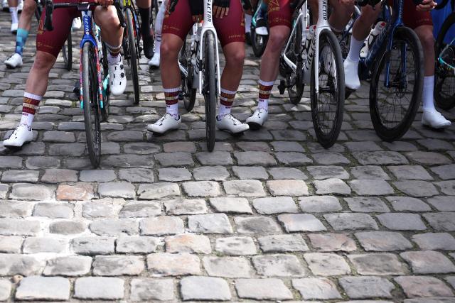Riders wait on cobblestone road at the start of the 123rd edition of the Paris-Roubaix one-day classic cycling race, 258.3 km between Compiègne and Roubaix, northern France, on April 12, 2026. (Photo by Anne-Christine POUJOULAT / AFP)