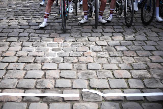 Riders wait on cobblestone road at the start of the 123rd edition of the Paris-Roubaix one-day classic cycling race, 258.3 km between Compiègne and Roubaix, northern France, on April 12, 2026. (Photo by Anne-Christine POUJOULAT / AFP)