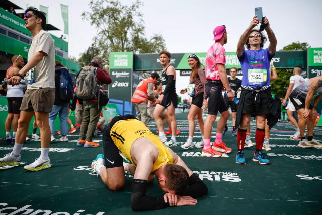 Participants react after crossing the finish line during the Paris Marathon, in Paris, on April 12, 2026. (Photo by Ian LANGSDON / AFP)