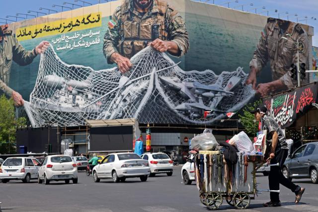 A vendor pushes his cart past a giant billboard reading 'The Strait of Hormuz remains closed' at the Revolution Square in Tehran on April 12, 2026. Iran's parliament speaker Mohammad Bagher Ghalibaf, who was part of peace talks with the United States this weekend, said on April 12 that Washington was "unable" to win Tehran's trust during the discussions. (Photo by ATTA KENARE / AFP) / 