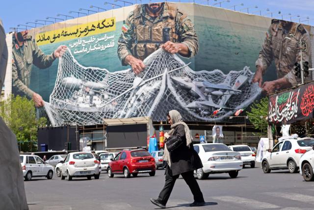 A woman walks past a giant billboard reading 'The Strait of Hormuz remains closed' at the Revolution Square in Tehran on April 12, 2026. Iran's parliament speaker Mohammad Bagher Ghalibaf, who was part of peace talks with the United States this weekend, said on April 12 that Washington was "unable" to win Tehran's trust during the discussions. (Photo by ATTA KENARE / AFP) / 