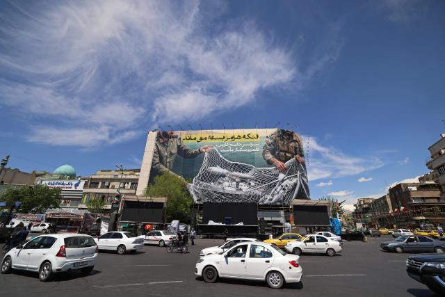 Commuters make their way past a giant billboard reading 'The Strait of Hormuz remains closed' at the Revolution Square in Tehran on April 12, 2026. Iran's parliament speaker Mohammad Bagher Ghalibaf, who was part of peace talks with the United States this weekend, said on April 12 that Washington was "unable" to win Tehran's trust during the discussions. (Photo by ATTA KENARE / AFP) / 