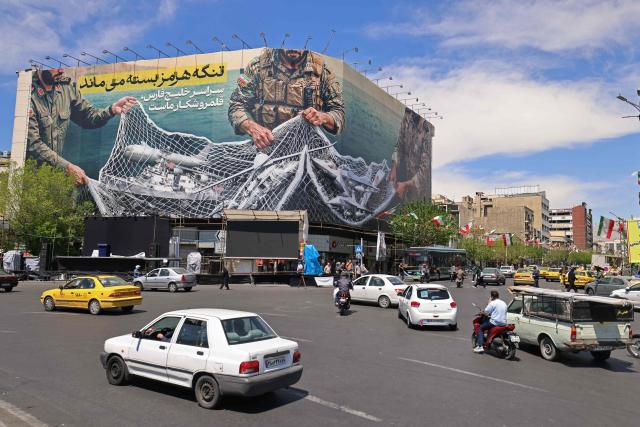 Motorists drive past a giant billboard reading 'The Strait of Hormuz remains closed' at the Revolution Square in Tehran on April 12, 2026. Iran's parliament speaker Mohammad Bagher Ghalibaf, who was part of peace talks with the United States this weekend, said on April 12 that Washington was "unable" to win Tehran's trust during the discussions. (Photo by ATTA KENARE / AFP) / 