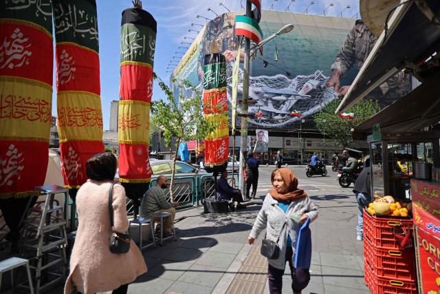 People walk along the roadside past at the Revolution Square in Tehran on April 12, 2026. Iran's parliament speaker Mohammad Bagher Ghalibaf, who was part of peace talks with the United States this weekend, said on April 12 that Washington was "unable" to win Tehran's trust during the discussions. (Photo by ATTA KENARE / AFP) / 
