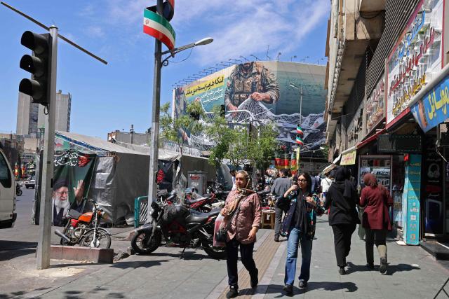 People walk along the roadside past at the Revolution Square in Tehran on April 12, 2026. Iran's parliament speaker Mohammad Bagher Ghalibaf, who was part of peace talks with the United States this weekend, said on April 12 that Washington was "unable" to win Tehran's trust during the discussions. (Photo by ATTA KENARE / AFP) / 