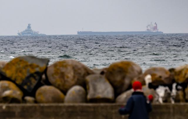 People watch the Swedish Coast Guard vessel KBV003 (L) and the boarded bulk carrier Hui Yuan outside the port of Kåseberga west of Ystad, Sweden, on Sunday 12 April 2026. The 225-meter-long bulk carrier Hui Yuan was on its way from Russia to Las Palmas and is suspected of environmental crimes after flushing coal residues into the sea. (Photo by Johan NILSSON / TT News Agency / AFP) / Sweden OUT