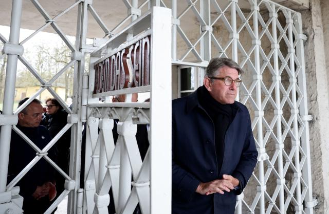 German State Minister for Culture and Media Wolfram Weimer (R) walks through the main gate with the inscription "Jedem das Seine" (To Each His Own) as he arrives at the memorial site of the former Nazi concentration camp Buchenwald on April 12, 2026, to attend the commemoration ceremony to mark the 81th anniversary of the liberation of the Buchenwald Nazi concentration camp at the camp's memorial site near Weimar, eastern Germany. From 1937 to 1945, almost 280,000 victims of the Nazis were imprisoned in Buchenwald concentration camp and its satellite camps; more than 56,000 were murdered or died as a result of inhumane conditions. Among the prisoners were Jews, Roma, domestic political opponents of the Nazis, and forced laborers from Eastern Europe. Buchenwald is one of the most symbolically significant and best-known former concentration camps in Germany. (Photo by Jens SCHLUETER / AFP)