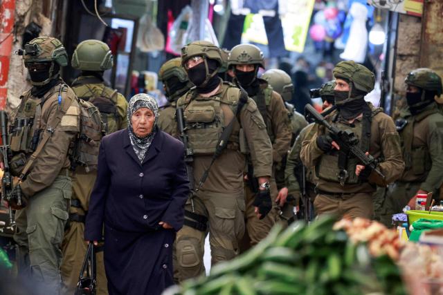A Palestinian woman walks past Israeli soldiers patrolling the market in the Old City of Nablus, in the northern Israeli-occupied West Bank on April 12, 2026. Israeli police said on April 12, eight suspects were arrested after an overnight attack by Israeli civilians on a Palestinian village in the occupied West Bank. Violence in the West Bank, which Israel has occupied since 1967, has risen sharply since the October 7, 2023 Hamas attack on Israel triggered the Gaza war. (Photo by Jaafar ASHTIYEH / AFP)