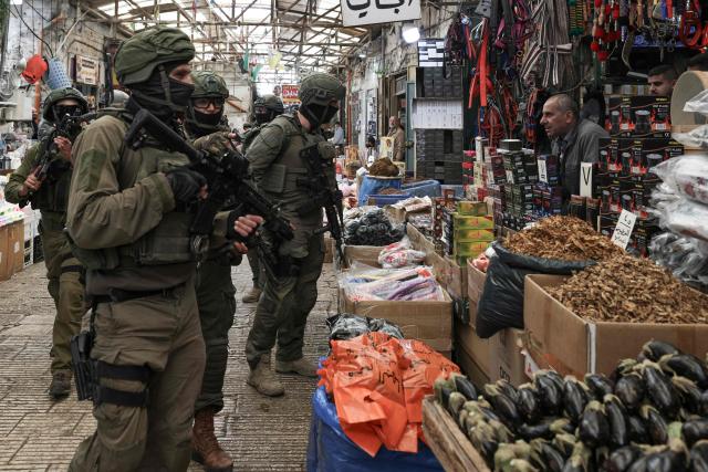 A shop keeper looks on as Israeli soldiers patrol through the market in the Old City of Nablus, in the northern Israeli-occupied Palestinian West Bank on April 12, 2026. Israeli police said on April 12, eight suspects were arrested after an overnight attack by Israeli civilians on a Palestinian village in the occupied West Bank. Violence in the West Bank, which Israel has occupied since 1967, has risen sharply since the October 7, 2023 Hamas attack on Israel triggered the Gaza war. (Photo by JAAFAR ASHTIYEH / AFP)