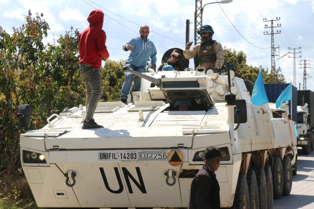 Civilians climb onto a United Nations Interim Force in Lebanon (UNIFIL) armored vehicle to take a selfie as they patrol the road in the southern Lebanese village of Tair Debba on April 12, 2026. Dozens of countries contributing troops to the UN peacekeeping force in Lebanon called on April 9, 2026, for a cessation of hostilities, after three blue helmets were killed as Israel and Hezbollah traded strikes. (Photo by Kawnat HAJU / AFP)