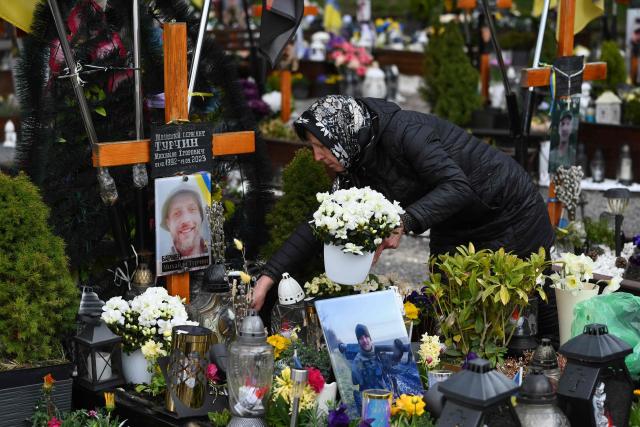 A woman lays flowers on the grave of a fallen Ukrainian soldier at the Lychakiv Military Cemetery during Orthodox Easter celebrations in Lviv on April 12, 2026, amid the Russian invasion of Ukraine. (Photo by YURIY DYACHYSHYN / AFP)