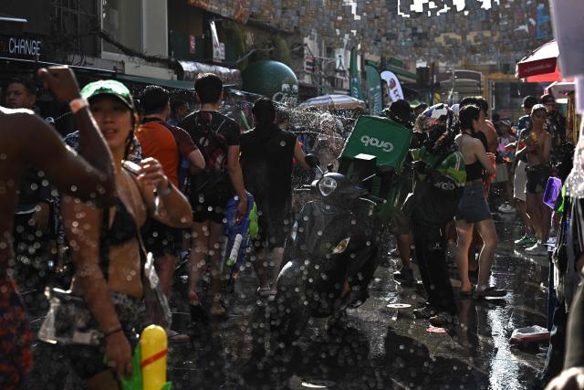 A Grab driver tries to complete a delivery order as revellers take part in mass water fights on the eve of the Songkran, or Thai New Year, on Khao San Road in Bangkok on April 12, 2026. (Photo by Lillian SUWANRUMPHA / AFP)