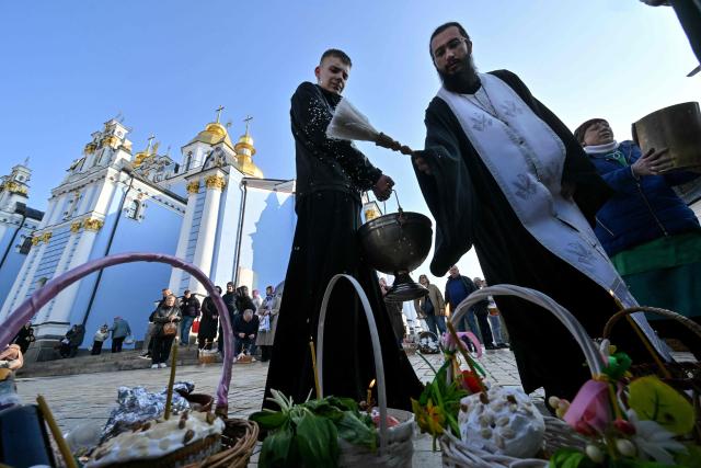 An Orthodox priest blesses believers and their baskets loaded with traditional cakes and eggs during Easter service outside Saint Michael's Golden-Domed Cathedral in Kyiv on April 12, 2026, amid the Russian invasion of Ukraine. Ukraine and Russia accused each other on April 12, 2026 of violating a truce in place for Orthodox Easter thousands of times, as the war dragged on into its fifth year. (Photo by Sergei SUPINSKY / AFP)