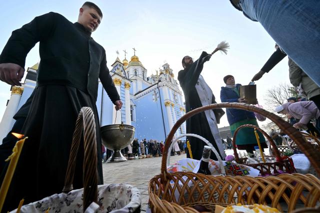 An Orthodox priest blesses believers and their baskets loaded with traditional cakes and eggs during Easter service outside Saint Michael's Golden-Domed Cathedral in Kyiv on April 12, 2026, amid the Russian invasion of Ukraine. Ukraine and Russia accused each other on April 12, 2026 of violating a truce in place for Orthodox Easter thousands of times, as the war dragged on into its fifth year. (Photo by Sergei SUPINSKY / AFP)
