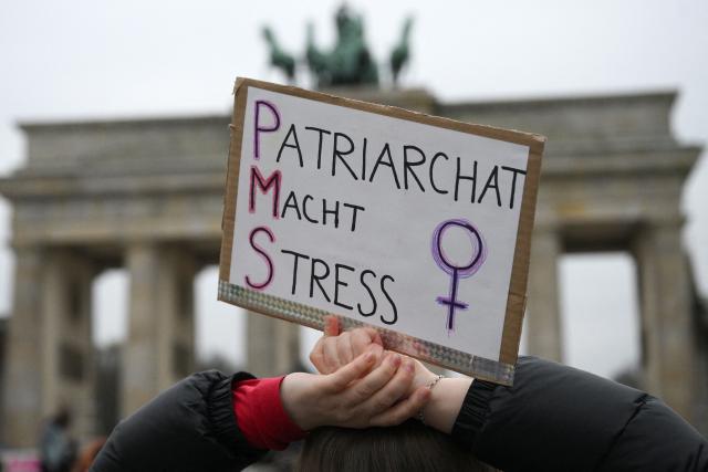 A participant holds up a placard with the lettering reading 'Patriarchy causes stress' during a demonstration against sexualized violence against women in front of Brandenburg Gate in Berlin on April 12, 2026. A feminist alliance has called for the demonstration, which is also held in support of German TV presenter and actress Collien Fernandes and all those affected to show: "Enough is enough! Stop the violence against women". The allegations from Fernandes against her ex-husband, actor Christian Ulmen, have sparked intense media debate about the "digital violence" increasingly perpetrated on the internet, mostly against women. The German government has responded to the outcry by pledging to introduce laws to punish the creation and distribution of sexualised deepfakes. (Photo by RALF HIRSCHBERGER / AFP)
