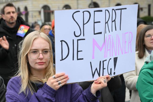A participant holds up a placard with the lettering reading 'Lock men away' during a demonstration against sexualized violence against women in front of Brandenburg Gate in Berlin on April 12, 2026. A feminist alliance has called for the demonstration, which is also held in support of German TV presenter and actress Collien Fernandes and all those affected to show: "Enough is enough! Stop the violence against women". The allegations from Fernandes against her ex-husband, actor Christian Ulmen, have sparked intense media debate about the "digital violence" increasingly perpetrated on the internet, mostly against women. The German government has responded to the outcry by pledging to introduce laws to punish the creation and distribution of sexualised deepfakes. (Photo by RALF HIRSCHBERGER / AFP)