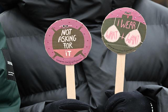 A participant hold up signs with the lettering reading 'Not asking for it - I wear what I want' during a demonstration against sexualized violence against women in Berlin on April 12, 2026. A feminist alliance has called for the demonstration, which is also held in support of German TV presenter and actress Collien Fernandes and all those affected to show: "Enough is enough! Stop the violence against women". The allegations from Fernandes against her ex-husband, actor Christian Ulmen, have sparked intense media debate about the "digital violence" increasingly perpetrated on the internet, mostly against women. The German government has responded to the outcry by pledging to introduce laws to punish the creation and distribution of sexualised deepfakes. (Photo by RALF HIRSCHBERGER / AFP)