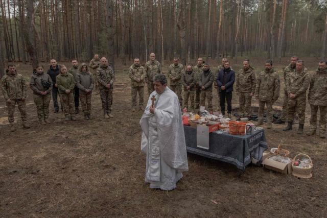Priest Petro Nemesh prays with Ukrainian military members of the 33rd separate mechanised brigade next to traditional cakes and other food to celebrate Orthodox Easter, in the Kharkiv region, on April 12, 2026, amid the Russian invasion of Ukraine. (Photo by Roman PILIPEY / AFP)