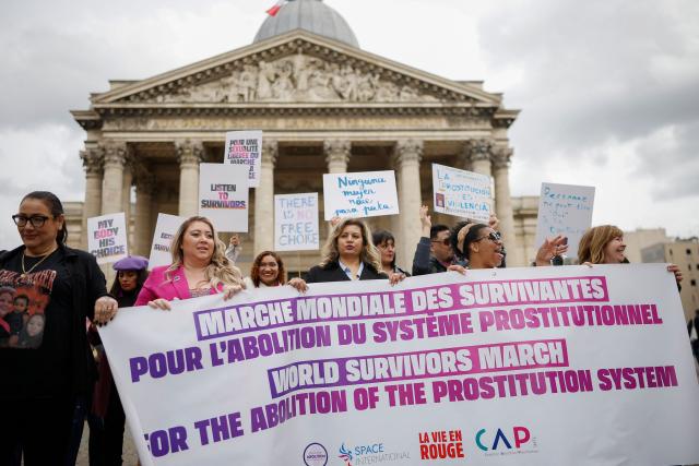 Protesters hold a banner and placards during a demonstration organised by the Collectif Abolition, a network of associations and activists aiming to end prostitution, on the occasion of the tenth anniversary of the prostitution law in France, in front of Pantheon in Paris on April 12, 2026. The 2016 French law made buying sex illegal, decriminalised sex workers, and created support programs to help them exit prostitution. (Photo by Ian LANGSDON / AFP)