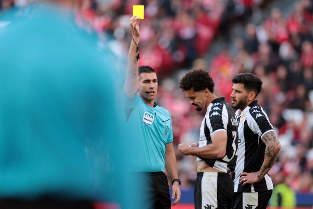 Portuguese referee Fabio Verissimo presents a yellow card to Nacional's Brazilian defender #34 Leo Santos (C) during the Portuguese League football match between SL Benfica and CD Nacional da Madeira at Luz Stadium in Lisbon on April 12, 2026. (Photo by PATRICIA DE MELO MOREIRA / AFP)