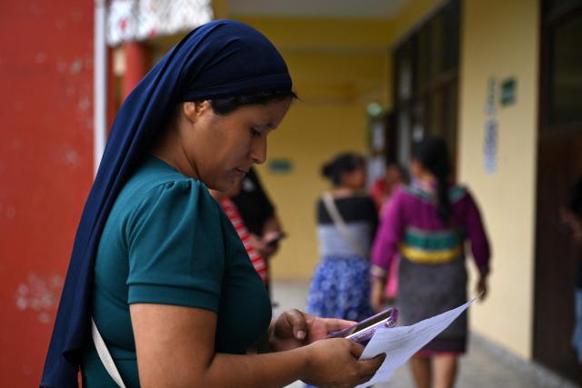 A member of the Evangelical Association of the Israelite Mission of the New Universal Covenant looks at her mobile phone outside a polling station in San Pablo de Tushmo, near Pucallpa, Uyacali region, Peru on April 12, 2026, during the presidential election. Peruvians will elect a new president from a record field of 35 candidates to lead a country plagued by organized crime and chronic political instability. (Photo by Hugo Alejos / AFP)