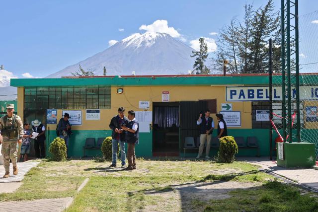 Employees of the National Office of Electoral Processes (ONPE), observers of the European Union and a member of the armed forces are seen outside a polling station in the district of Chiguata, an agricultural area located some 25 kilometres from Arequipa, Peru on April 12, 2026, during general elections. Peruvians will elect a new president from a record field of 35 candidates to lead a country plagued by organized crime and chronic political instability. (Photo by Diego RAMOS / AFP)