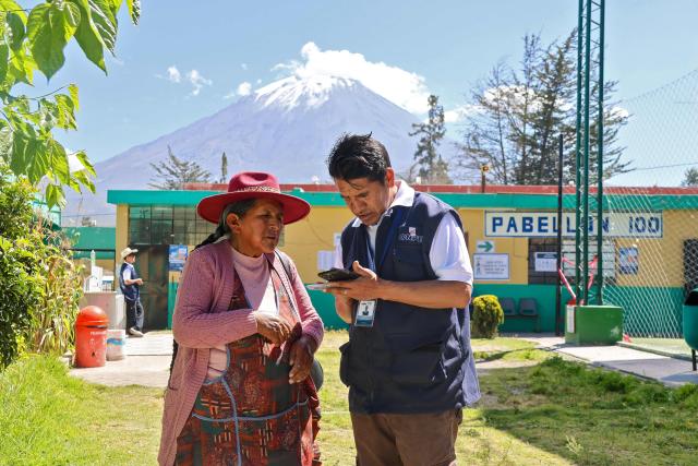 A peasant woman is helped by an employee of the National Office of Electoral Processes (ONPE) in the district of Chiguata, an agricultural area located some 25 kilometres from Arequipa, Peru on April 12, 2026, during general elections. Peruvians will elect a new president from a record field of 35 candidates to lead a country plagued by organized crime and chronic political instability. (Photo by Diego RAMOS / AFP)