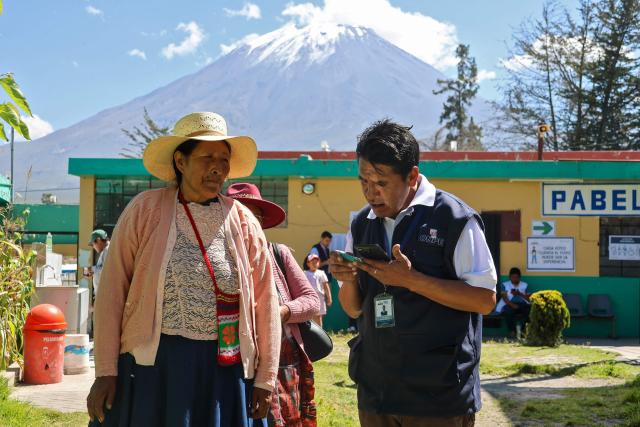 A peasant woman is helped by an employee of the National Office of Electoral Processes (ONPE) in the district of Chiguata, an agricultural area located some 25 kilometres from Arequipa, Peru on April 12, 2026, during general elections. Peruvians will elect a new president from a record field of 35 candidates to lead a country plagued by organized crime and chronic political instability. (Photo by Diego RAMOS / AFP)