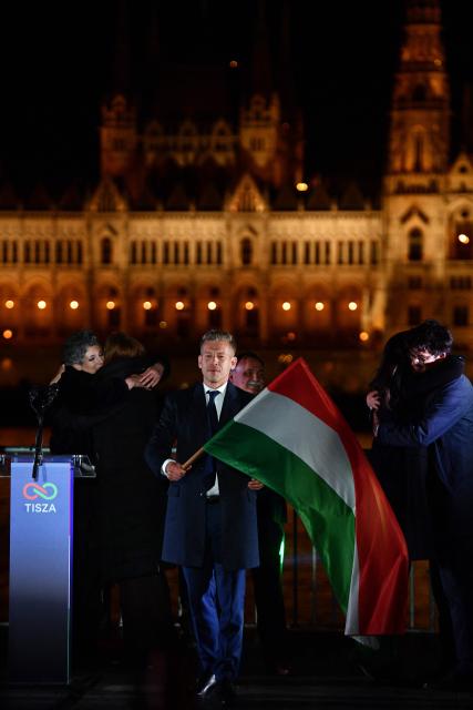Peter Magyar, leader of the pro-European conservative TISZA party, waves the national flag on the banks on the river Danube with the Parliament building in the background, during their election night party in Budapest during the general election in Hungary, on April 12, 2026. Polls closed in Hungary's parliamentary election, with turnout reaching a record high in the crunch vote that sees nationalist Prime Minister Viktor Orban's 16-year stint in power face an unprecedented challenge from conservative political newcomer Peter Magyar. (Photo by Ferenc ISZA / AFP)