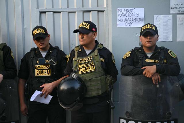 Members of Peru’s police force stand guard at the Virgen de la Asuncion school, where the polling station is closed, in Pamplona Alta, in the San Juan de Miraflores district on the outskirts of Lima, on April 12, 2026. Hours-long delays marred Peru's presidential and legislative elections on April 12, as voters sought to end political chaos that has seen a string of presidents ousted or jailed. (Photo by Ernesto BENAVIDES / AFP)