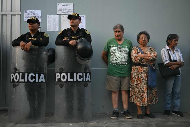 Members of Peru’s police force stand guard next to people at the Virgen de la Asuncion school, where the polling station is closed, in Pamplona Alta, in the San Juan de Miraflores district on the outskirts of Lima, on April 12, 2026. Hours-long delays marred Peru's presidential and legislative elections on April 12, as voters sought to end political chaos that has seen a string of presidents ousted or jailed. (Photo by Ernesto BENAVIDES / AFP)
