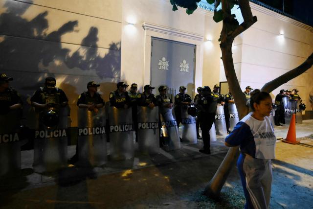 Police officers stand guard outside the National Jury of Elections (JNE) headquarters as demonstrators protest following the first results of the presidential election in Lima on April 12, 2026. Right-wing candidate Keiko Fujimori led exit polls following Peru's troubled presidential election on April 12, 2026, but failed to avoid a runoff after a tight vote marred by irregularities and a police raid on the country's election authority. (Photo by Luis ROBAYO / AFP)