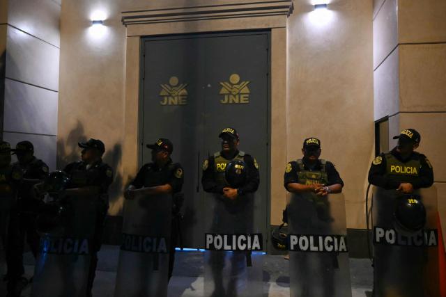 Police officers stand guard outside the National Jury of Elections (JNE) headquarters as demonstrators protest following the first results of the presidential election in Lima on April 12, 2026. Right-wing candidate Keiko Fujimori led exit polls following Peru's troubled presidential election on April 12, 2026, but failed to avoid a runoff after a tight vote marred by irregularities and a police raid on the country's election authority. (Photo by Luis ROBAYO / AFP)