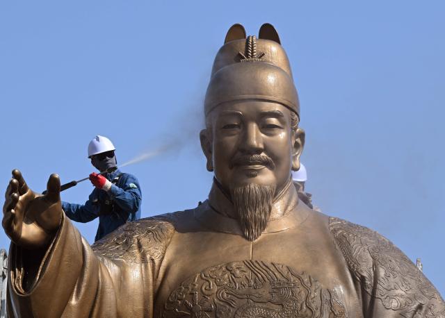 A worker sprays water to wash the bronze statue of King Sejong, the 15th-century Korean king, during a spring cleaning event at Gwanghwamun Square in Seoul on April 13, 2026. (Photo by Jung Yeon-je / AFP)