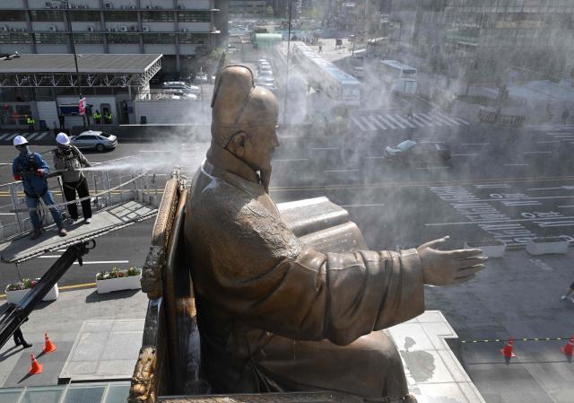 A worker sprays water to wash the bronze statue of King Sejong, the 15th-century Korean king, during a spring cleaning event at Gwanghwamun Square in Seoul on April 13, 2026. (Photo by Jung Yeon-je / AFP)