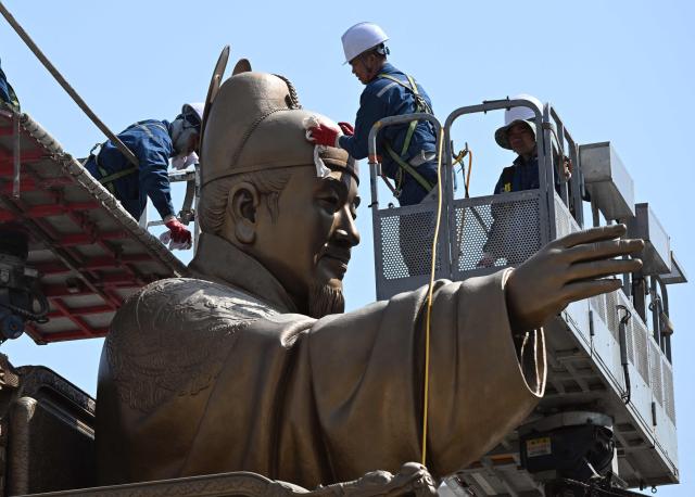 Workers wipe the bronze statue of King Sejong, the 15th century Korean king, during a spring cleaning event at Gwanghwamun Square in Seoul on April 13, 2026. (Photo by Jung Yeon-je / AFP)