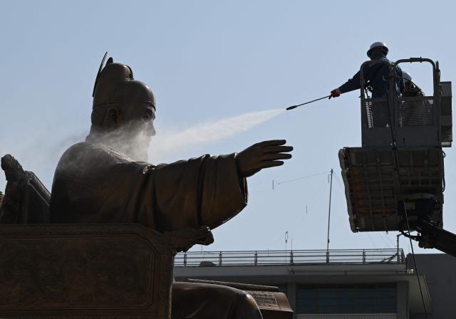 A worker sprays water to wash the bronze statue of King Sejong, the 15th-century Korean king, during a spring cleaning event at Gwanghwamun Square in Seoul on April 13, 2026. (Photo by Jung Yeon-je / AFP)
