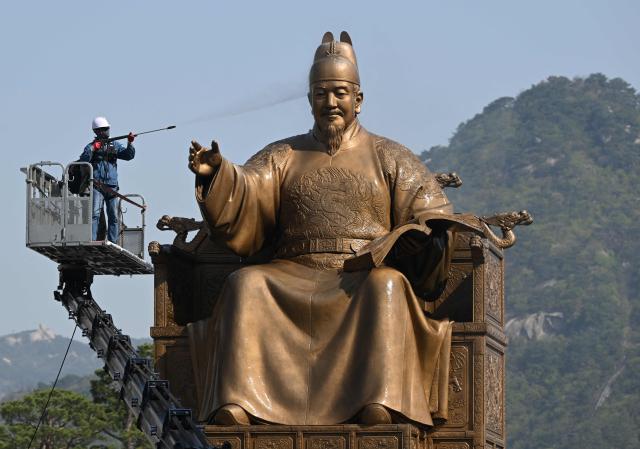 A worker sprays water to wash the bronze statue of King Sejong, the 15th-century Korean king, during a spring cleaning event at Gwanghwamun Square in Seoul on April 13, 2026. (Photo by Jung Yeon-je / AFP)