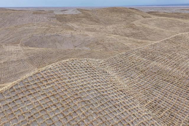 Workers set up straw barriers on rolling sand dunes at a desertification control area in Qingshui, Jiuquan in China's northwest Gansu province on April 12, 2026. (Photo by CN-STR / AFP) / China OUT