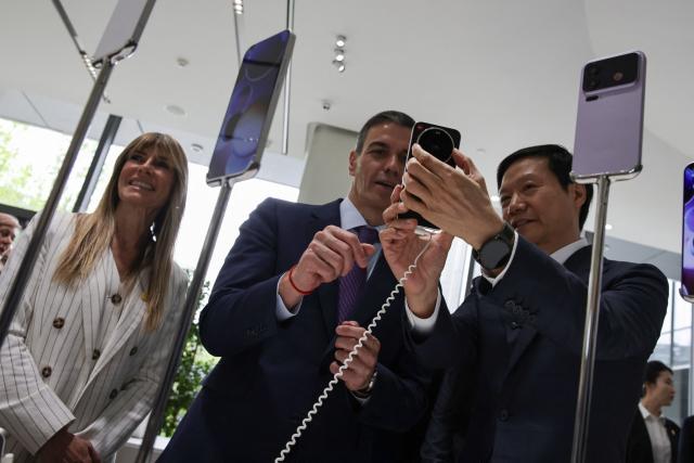 Founder, Chairman & CEO of Xiaomi, Lei Jun (R), shows a Xiaomi smartphone to Spain's Prime Minister Pedro Sanchez (C) at the Xiaomi headquarters in Beijing on April 13, 2026. Sanchez called China's trade imbalance with the European Union "unsustainable" on April 13, as he began a three-day visit to Beijing where he hopes to strengthen economic ties. (Photo by ANDRES MARTINEZ CASARES / POOL / AFP)