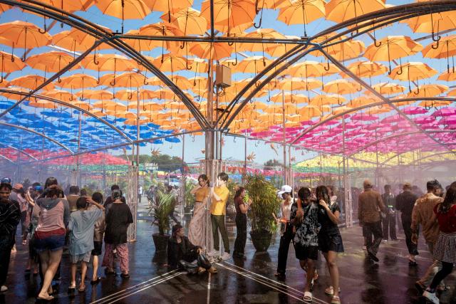 People walk under sprinklers during celebrations for Myanmar's Buddhist New Year water festival, also known as Thingyan, in Yangon on April 13, 2026. (Photo by Sai Aung MAIN / AFP)