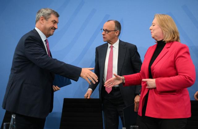 Bavaria's State Premier and leader of the conservative Christian Social Union (CSU) Markus Soeder and German Minister for Labour and Social Affairs Baerbel Bas (SPD) are about to shake hands as German Chancellor Friedrich Merz (C) looks on at the end of a press briefing on the results of their overnight coalition committee consultations, on April 13, 2026 at the Chancellery in Berlin. Chancellor Friedrich Merz said that Germany would cut petrol and diesel taxes for two months to provide relief to households and businesses hit by the energy shock during the Middle East war. (Photo by RALF HIRSCHBERGER / AFP)