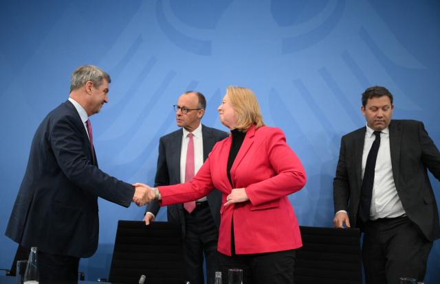 Bavaria's State Premier and leader of the conservative Christian Social Union (CSU) Markus Soeder and German Minister for Labour and Social Affairs Baerbel Bas (SPD) shake hands as German Chancellor Friedrich Merz (2ndL) and German Finance Minister and Vice Chancellor Lars Klingbeil (SPD, R) look on at the end of a press briefing on the results of their overnight coalition committee consultations, on April 13, 2026 at the Chancellery in Berlin. Chancellor Friedrich Merz said that Germany would cut petrol and diesel taxes for two months to provide relief to households and businesses hit by the energy shock during the Middle East war. (Photo by RALF HIRSCHBERGER / AFP)