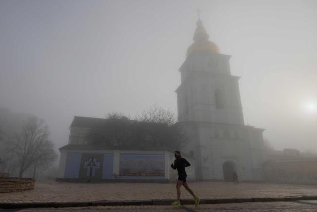 A local resident runs near St. Michael's Golden-Domed Monastery on a foggy morning in Kyiv, on April 13, 2026, amid the Russian invasion of Ukraine. (Photo by Tetiana DZHAFAROVA / AFP)